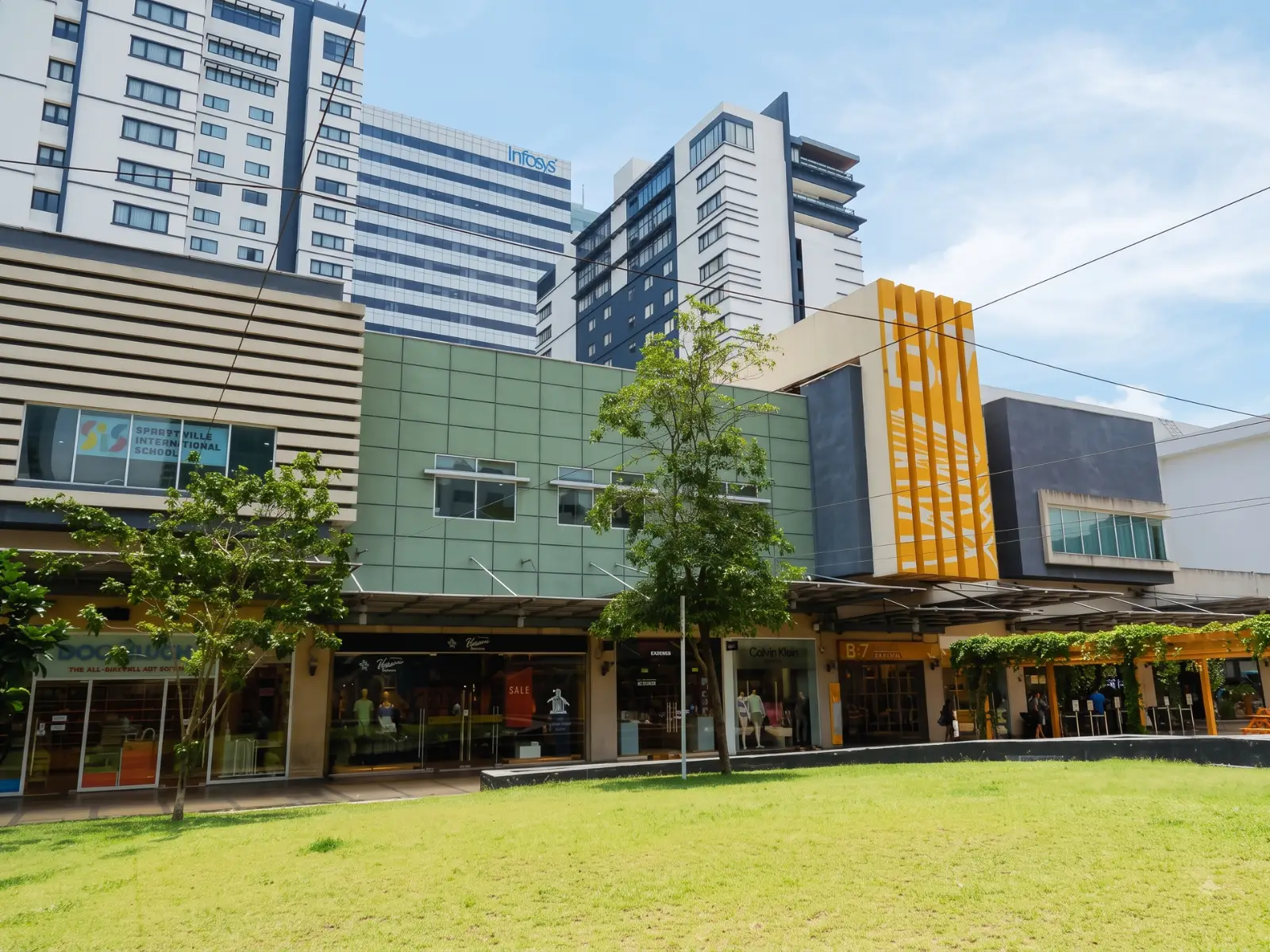 Street-level view of the modern commercial building facade housing Sproutville International School, featuring a distinctive green storefront and nearby landscaping.