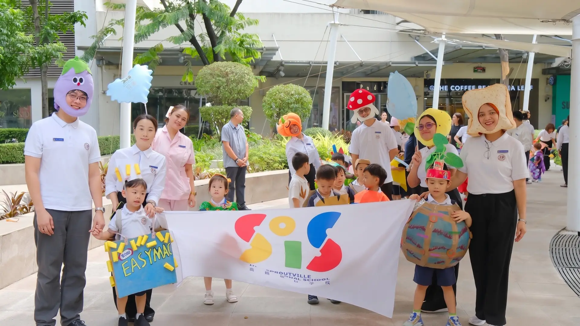 Teachers and students wearing creative food costumes holding a school banner during the outdoor Nutrition Month parade at Sproutville International School.