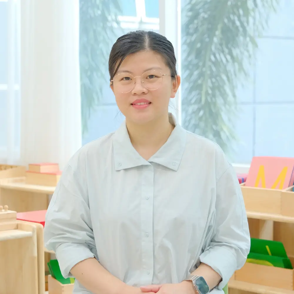 A smiling mother, Samsam's mom, sitting in a bright and organized Montessori classroom at Sproutville International School.