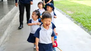 Joyful young students in uniform holding a walking rope during a guided morning walk on the outdoor campus path at Sproutville International School.