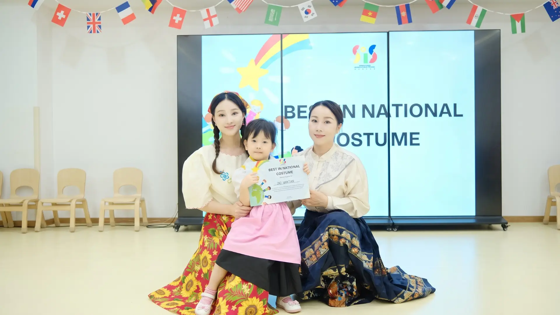 Young student receiving the Best in National Costume award alongside teachers in traditional dress during the United Nations celebration at Sproutville International School.